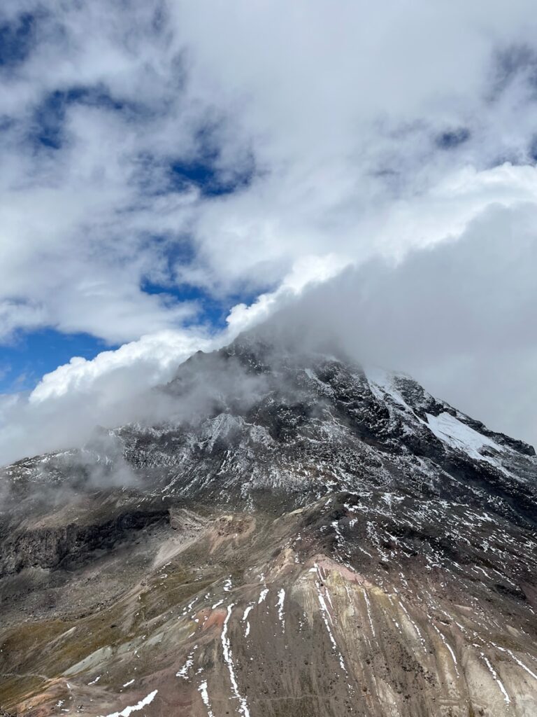 A very tall mountain covered in snow under a cloudy sky